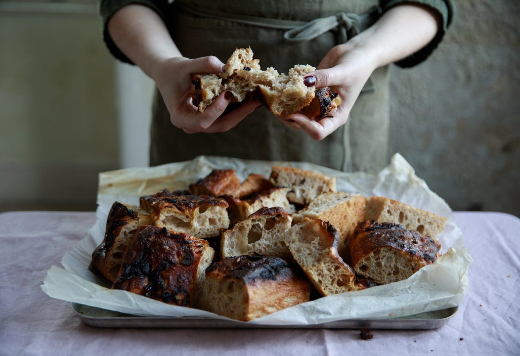 Hands tearing fresh baked bread from a tray on a table with a white tablecloth