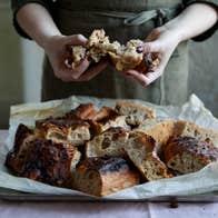 Hands tearing fresh baked bread from a tray on a table with a white tablecloth