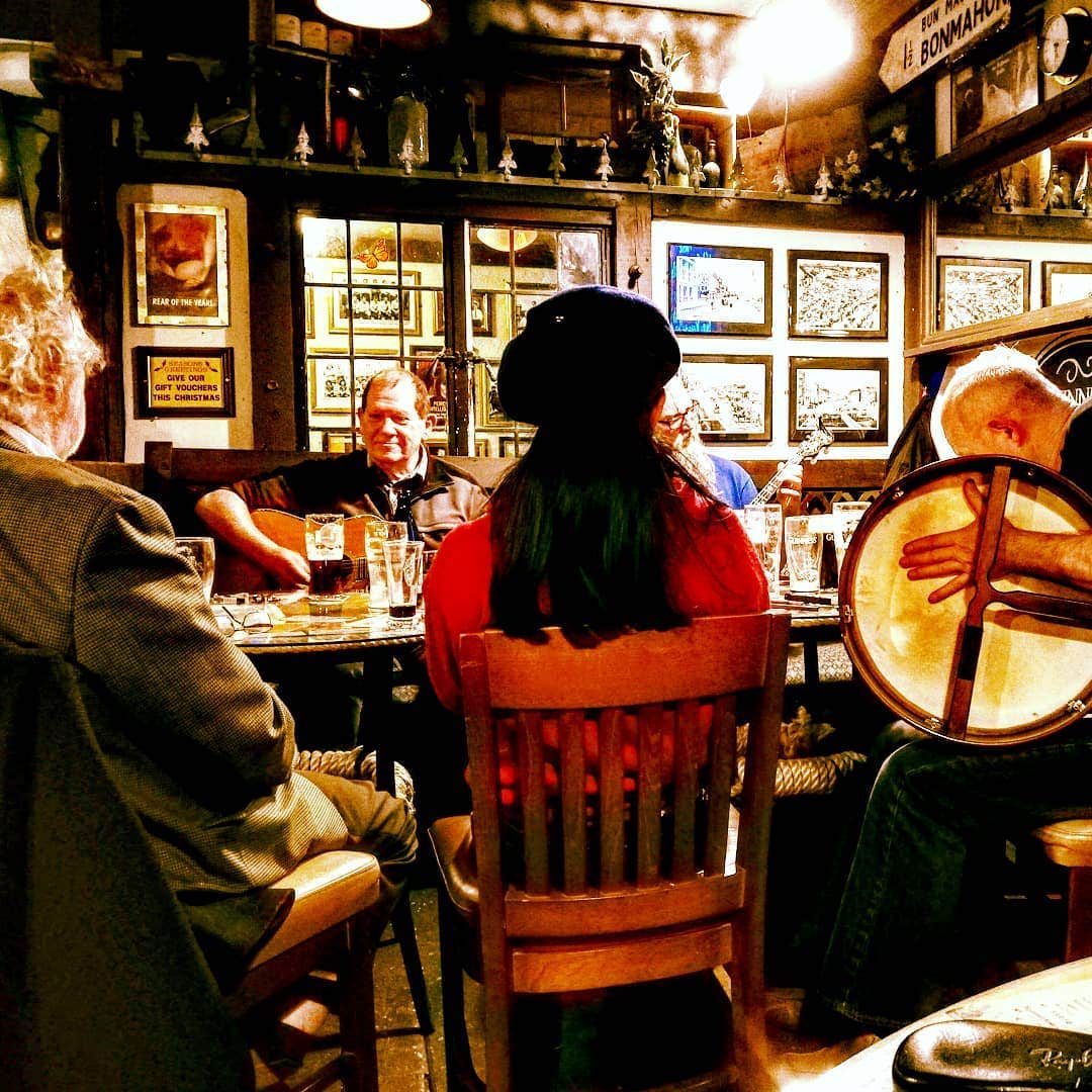 People gathered around a table in a traditional Irish pub with instruments and pints of Guinness on the table in front of them.