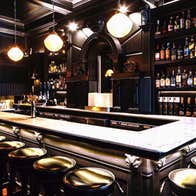 A rectangular cocktail bar surrounded by empty bar stools in a low light environment