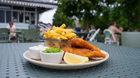 A plate of fish and chips with peas and a lemon slice