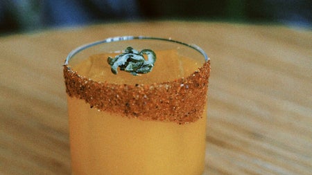 Shot glass with an orange coloured drink and spices along the edge