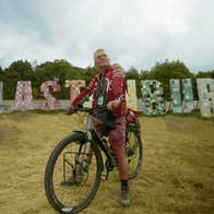 A man looking wistful on a bike with large letters in the background spelling out a name of a town