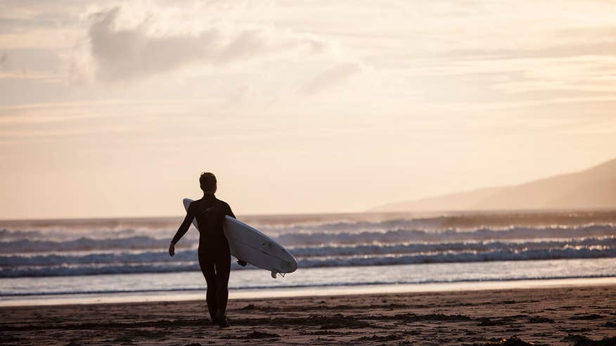 A surfer in a wetsuit heading towards the sea at Inch Beach, Co. Kerry