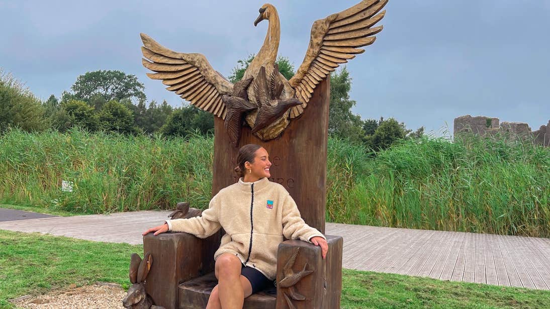 Roz Purcell sitting on a wooden chair carved with animal sculptures on the grounds of Roscommon Castle, Roscommon