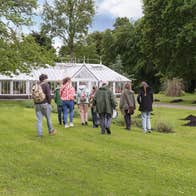 People walking across grass to an old glass house.