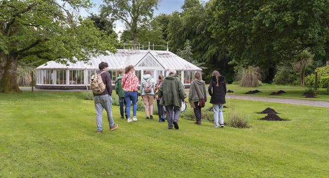 People walking across grass to an old glass house.