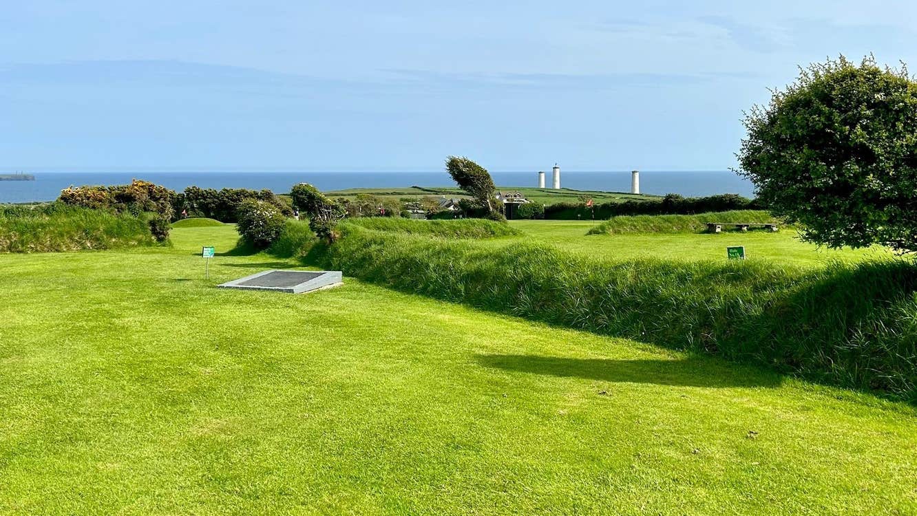 Golf green and trees with the ocean and a blue sky in the background