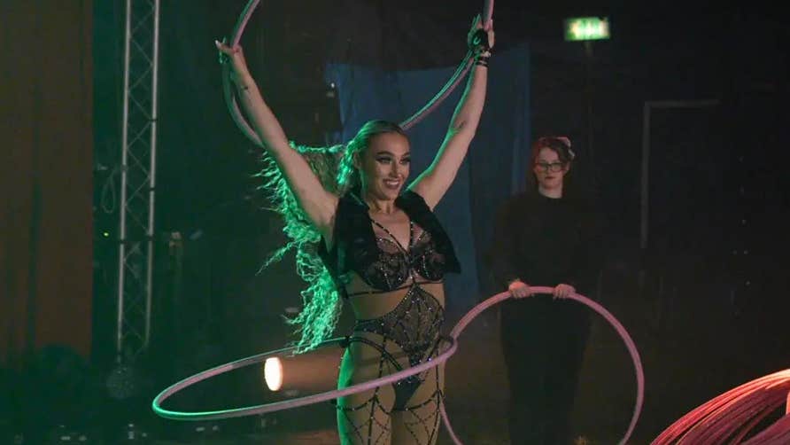 A smiling woman in a circus ring holding up hoola hoop
