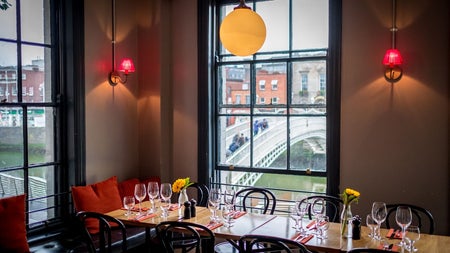 A restaurant with tables prepared for diners with old style windows and views of a bridge