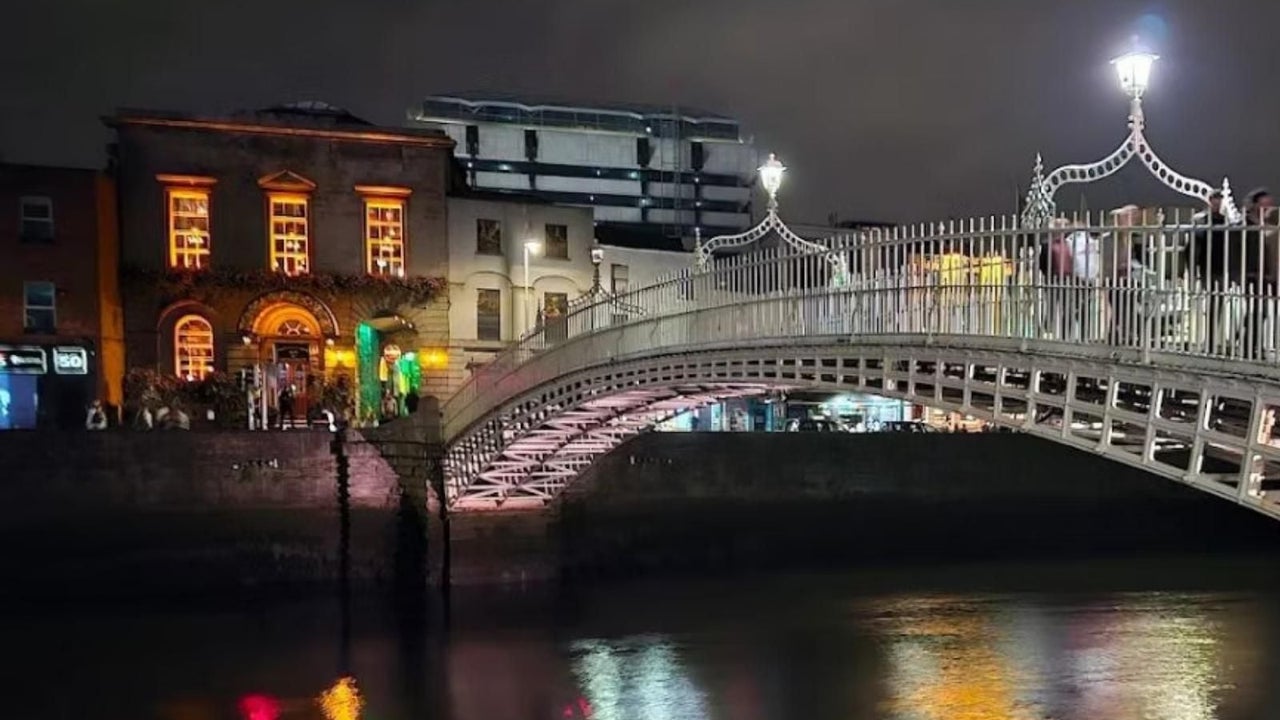 A nightscape of a bridge spanning a river with buildings on the opposite side