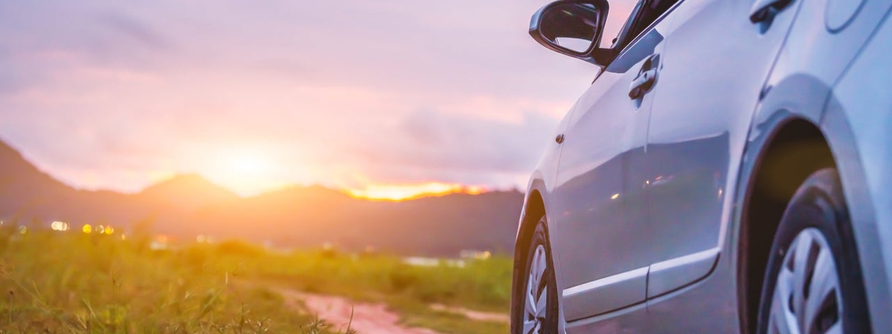 Small car on a country lane facing the setting sun