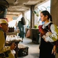 A girl with a chicken is talking a man at a market stall.