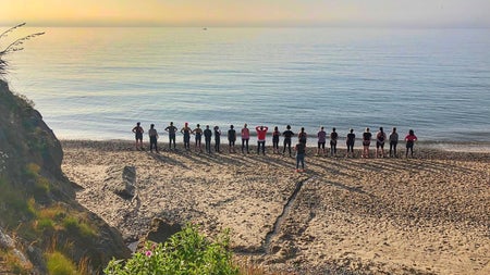 A group standing on sand by the sea watching the sunrise in the distance