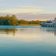 A boat sailing down a calm river near the shore on the Shannon