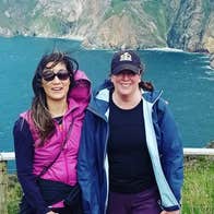 Two ladies standing on a platform with the sea and cliffs behind them