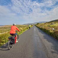 Two cyclists on a country road lined with stone walls and a coastal view