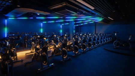 Rows of exercise bikes in a gym under blue lighting