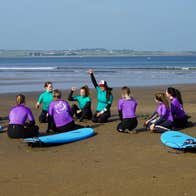Group of surf students with surfboards sitting in a circle on the beach during a lesson