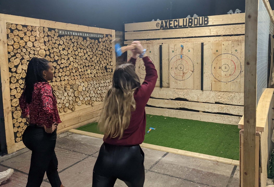 Two people one holding an axe in an axe throwing wooden area with targets in front