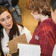 A woman with a clipboard is talking to 2 young children