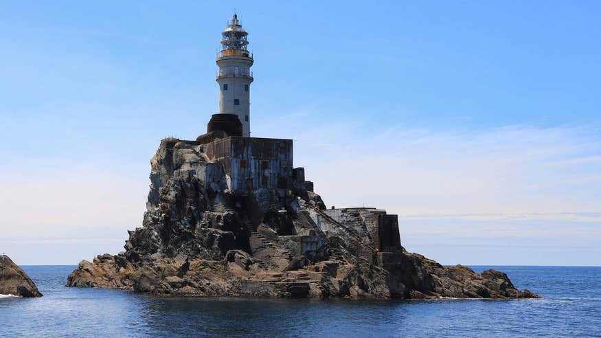 Fastnet Lighthouse on a clear day with blue skies and calm water all around