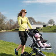 Man on a bike with a child while a woman pushes a child on a buggy beside a river