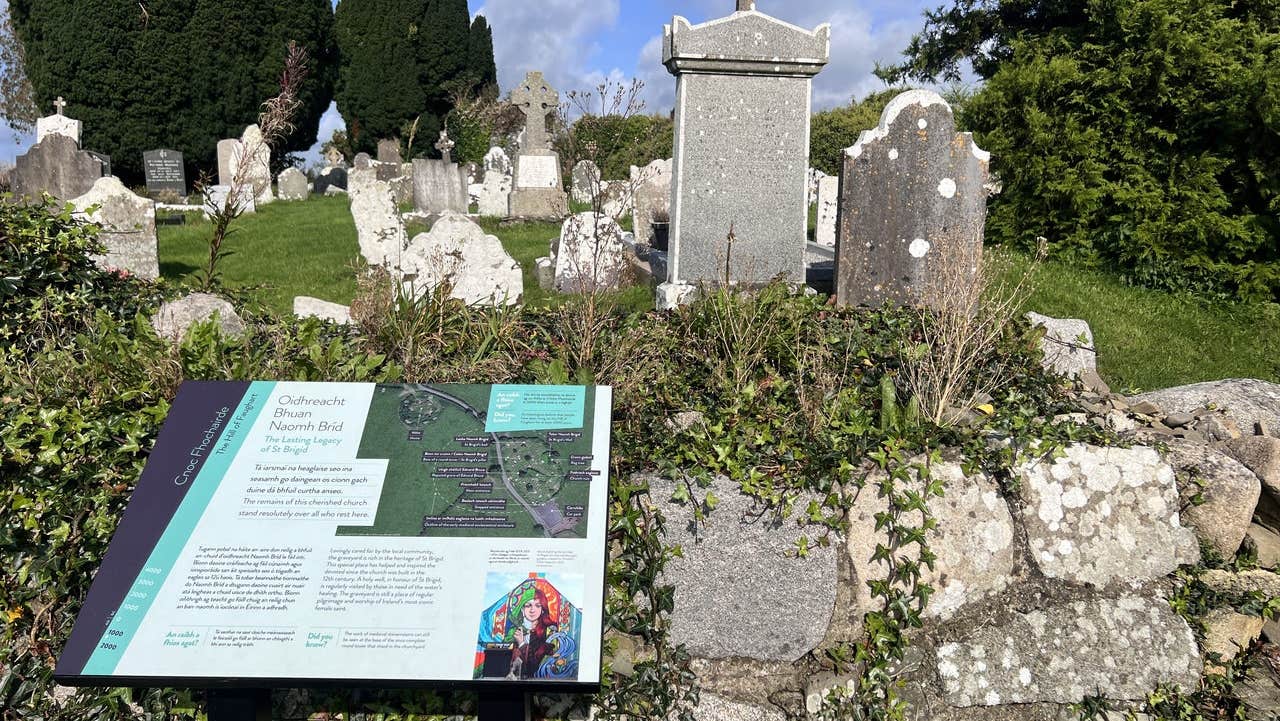 View over wall of a cemetery with a story board and old headstones