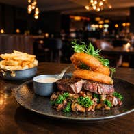 Steak with onion rings and a sauce on a plate with a portion of chips in the background