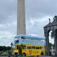 Vintage Tea Trips Bus at Glasnevin Cemetery, an old fashioned double decker bus park in a cemetery with tall thin round tower.