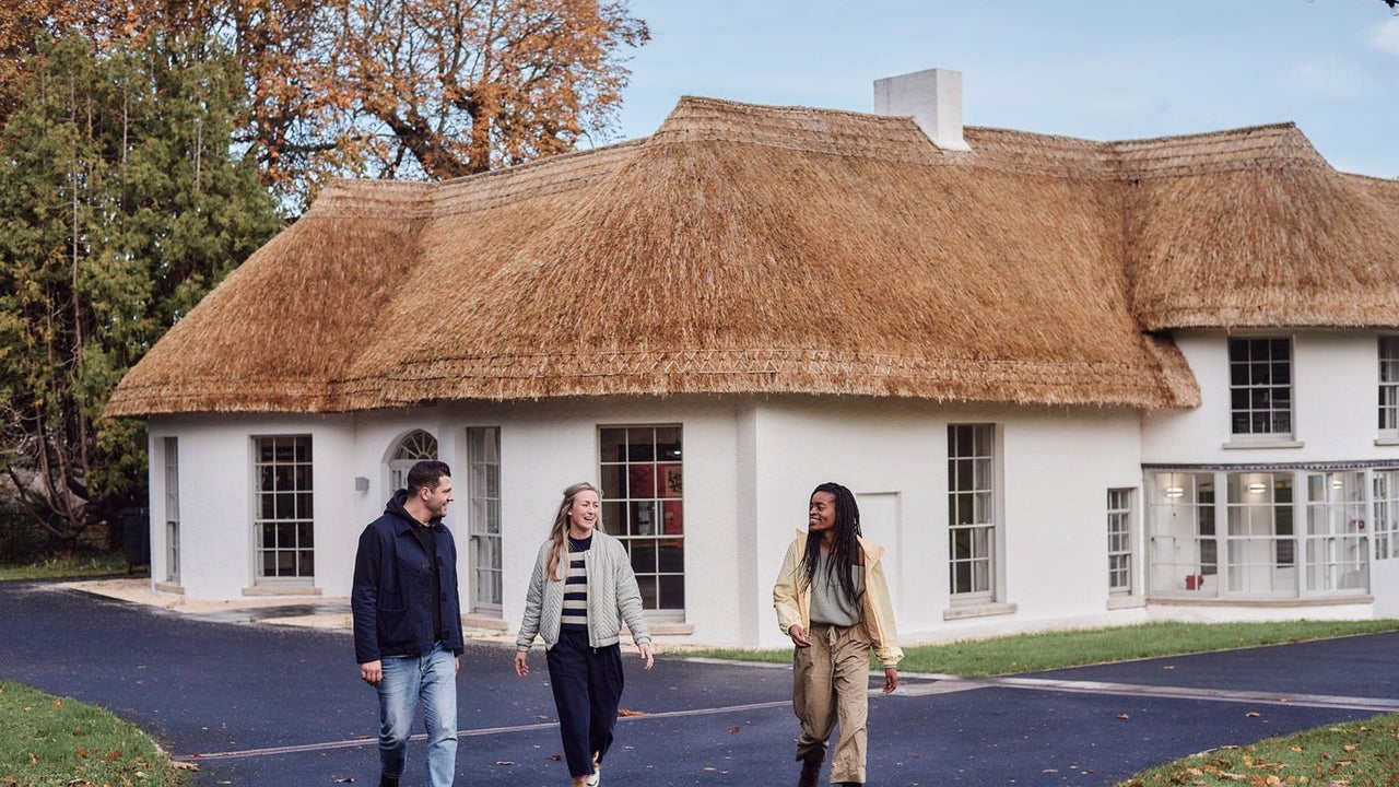 Three people walking away from a white building with a thatched roof