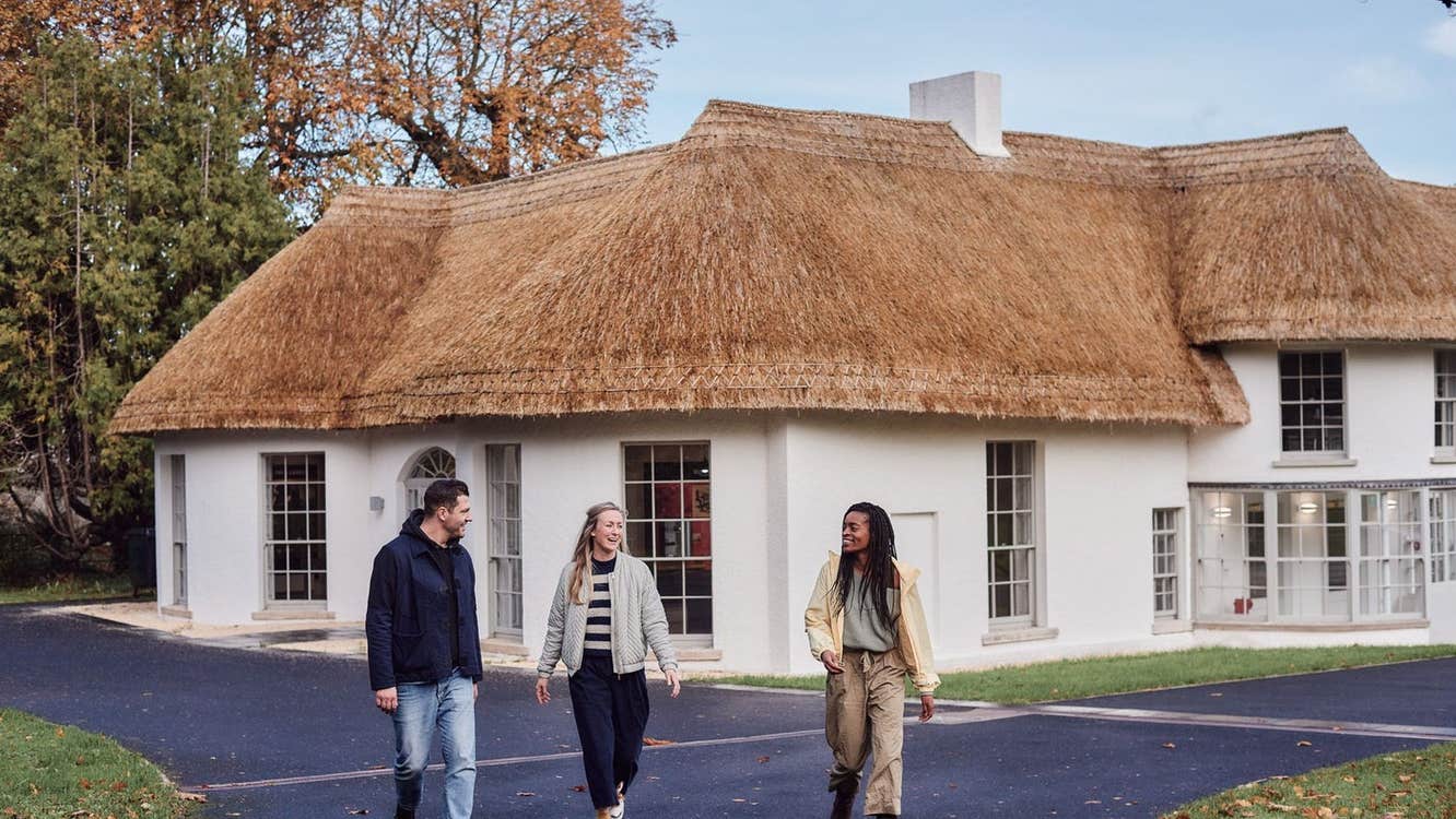 Three people walking away from a white building with a thatched roof