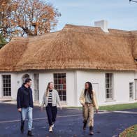 Three people walking away from a white building with a thatched roof
