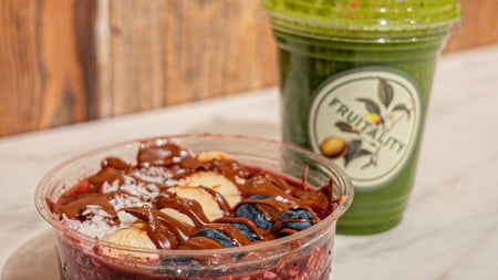 A close up of a bowl with seeds and fruit and a plastic smoothie cup with a business logo