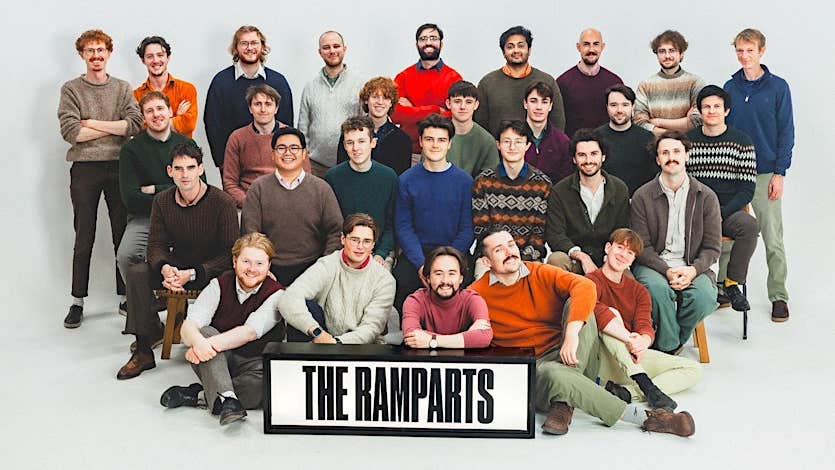 A large group of smiling men, some seated, the rest standing, against plain white background.