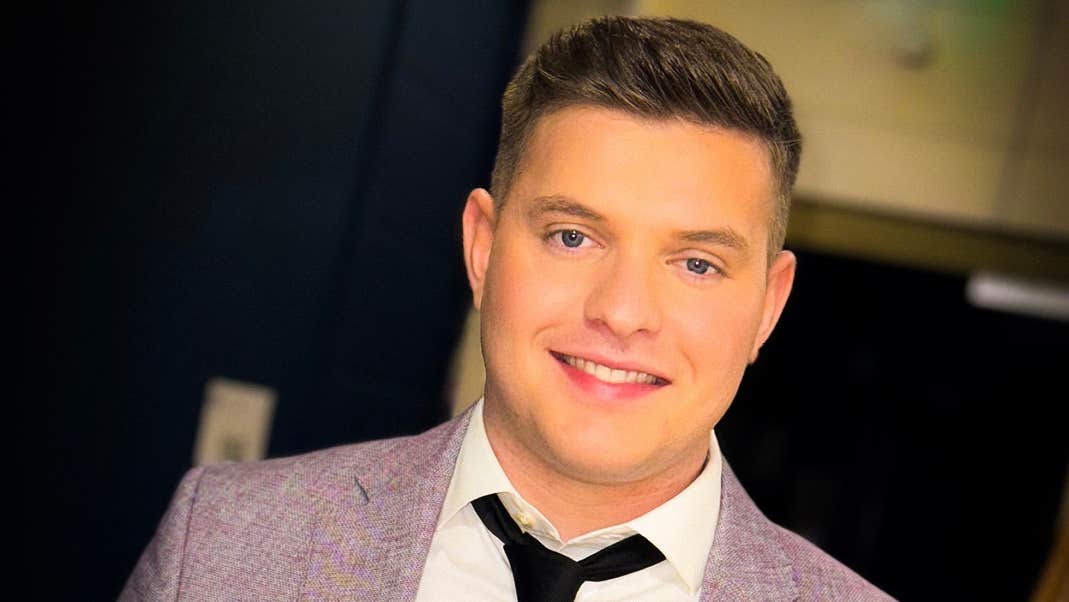 A smiling man in grey jacket and loose black tie