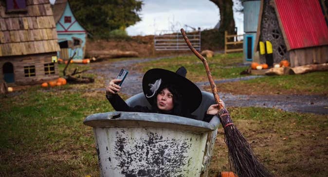 A person with large black hat and broom is in a large grey container taking a selfie.