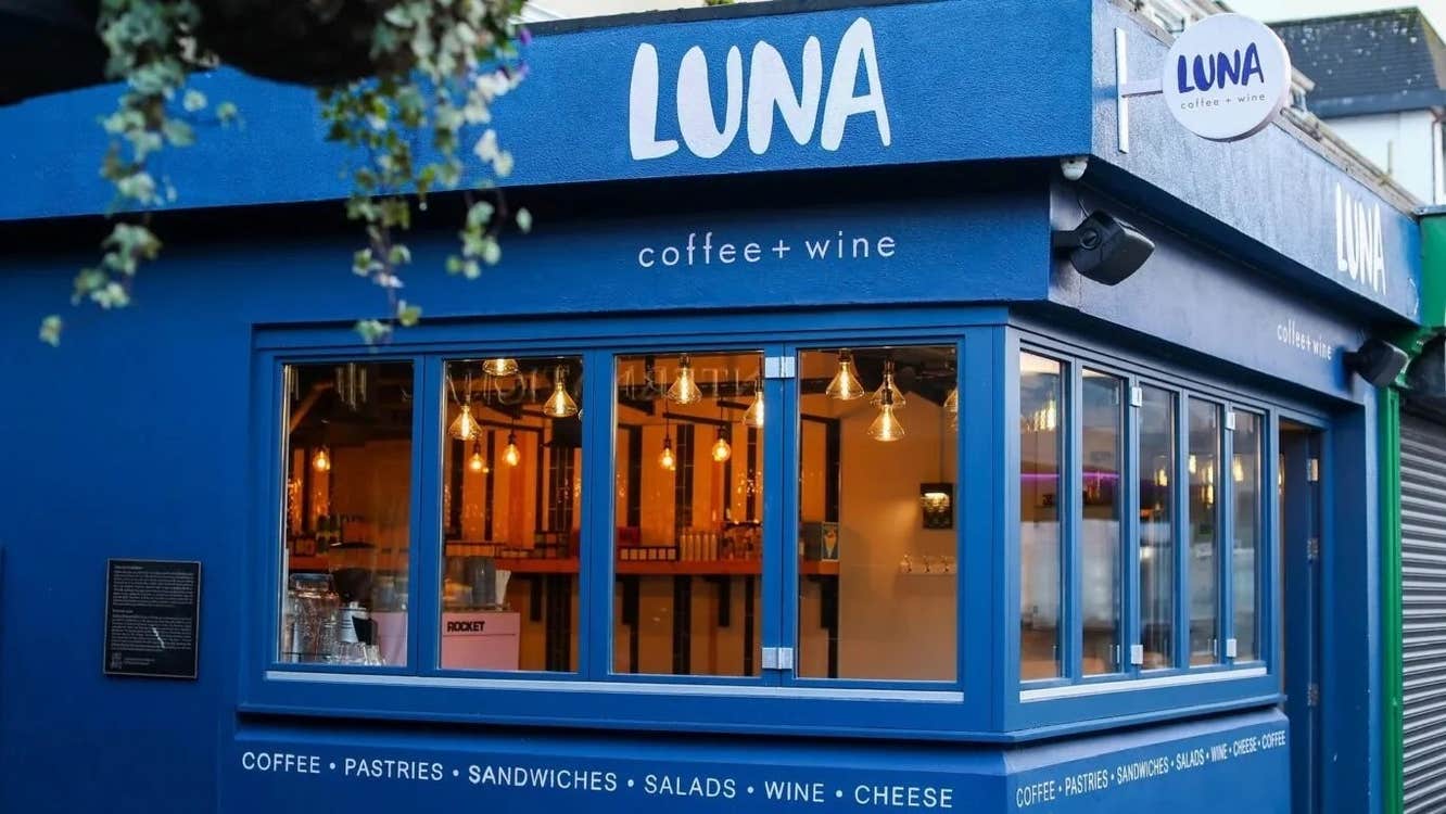 Exterior of café with several long narrow windows with a hanging basket of plants
