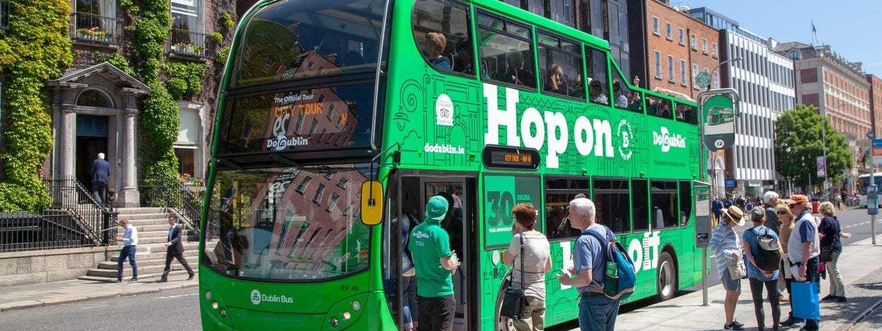 A large green double decker bus with people queueing to get on it