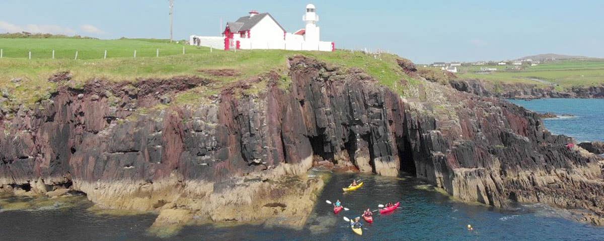Irish Adventures kayakers in the sea below cliffs and a lighthouse