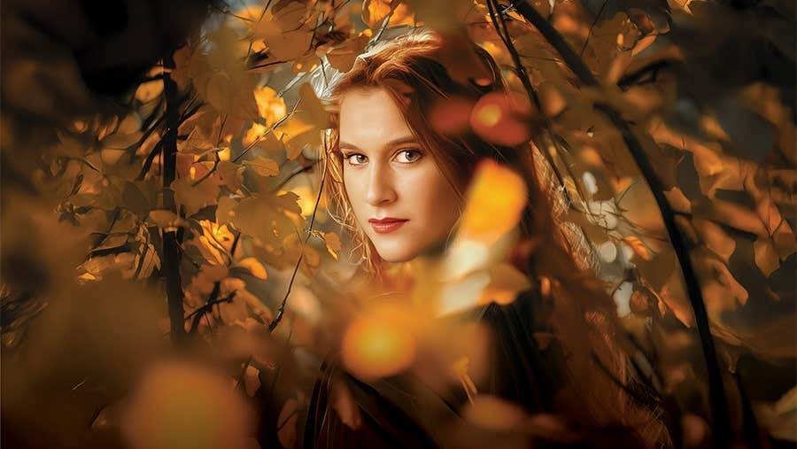 The Cunning Little Vixen, Irish National Opera, the face of a woman viewed through golden and orange autumn leaves
