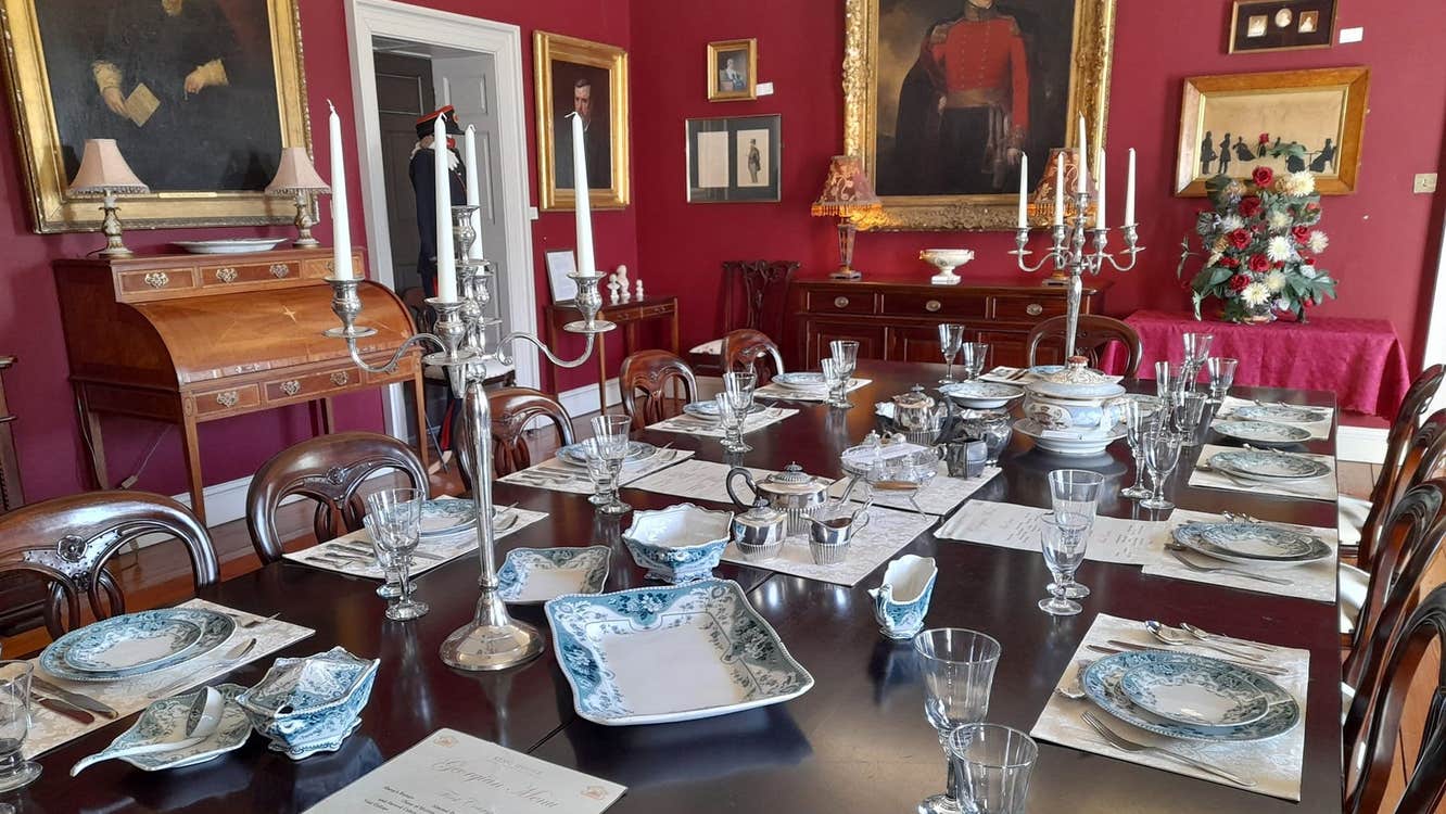 Large dining table set for service in a room with red walls and painting hanging on them