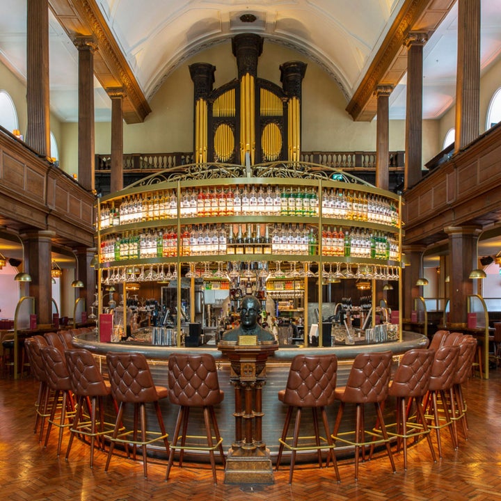 A circular bar with chairs around it and a display of bottles behind the bar