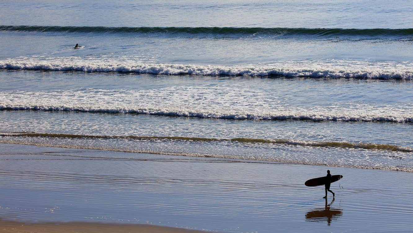 A surfer walking along Inch Strand in County Kerry with their surfboard.