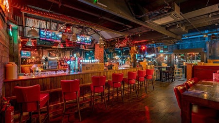 Interior of a pub with red chairs at the bar and tables set for service