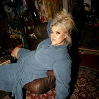 A woman in a blue denim dress is laying draped across a chair