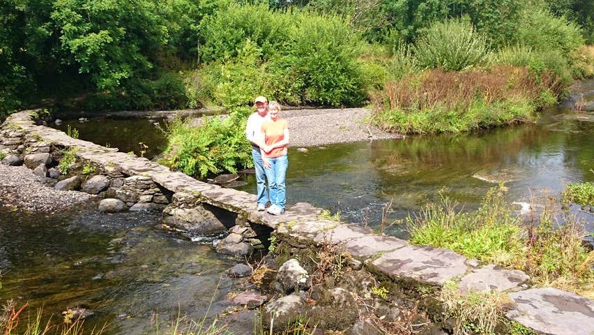 A couple standing on a small stone wall on a river