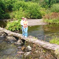 A couple standing on a small stone wall on a river