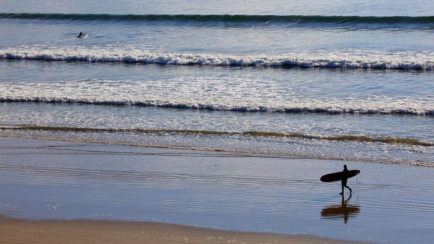 Person walking down the beach with surfboard under their arm with ocean waves behind them on Inch Strand.