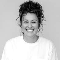 A broadly smiling woman with plain top and background.